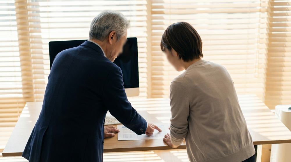 デスクで若手社員に資料を示しながら教える先輩社員